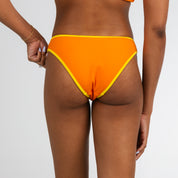 A model showcases Honey Swims Marigold Terry | Classic Bottoms, vibrant orange bikini bottoms with yellow trim, against a plain white background, shown from the waist down.