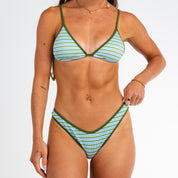 A woman models the Piper Ribbed Triangle Set bikini by Honey Swim in green and white with adjustable straps, minimal jewelry, and her face not shown, against a plain white background.